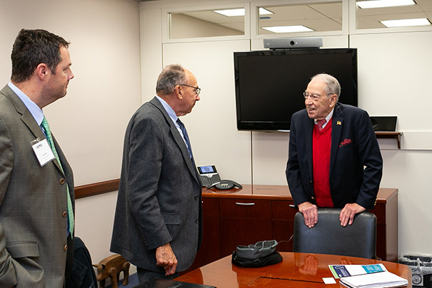 Three men stand talking around a conference room table