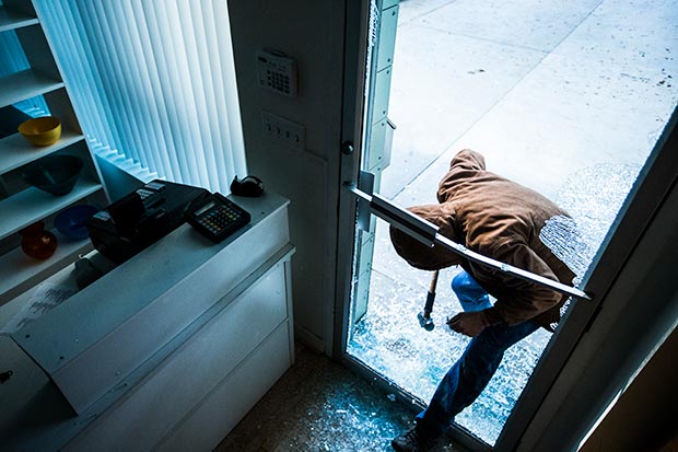 A robber using a sledgehammer to break the glass of a business establishment.