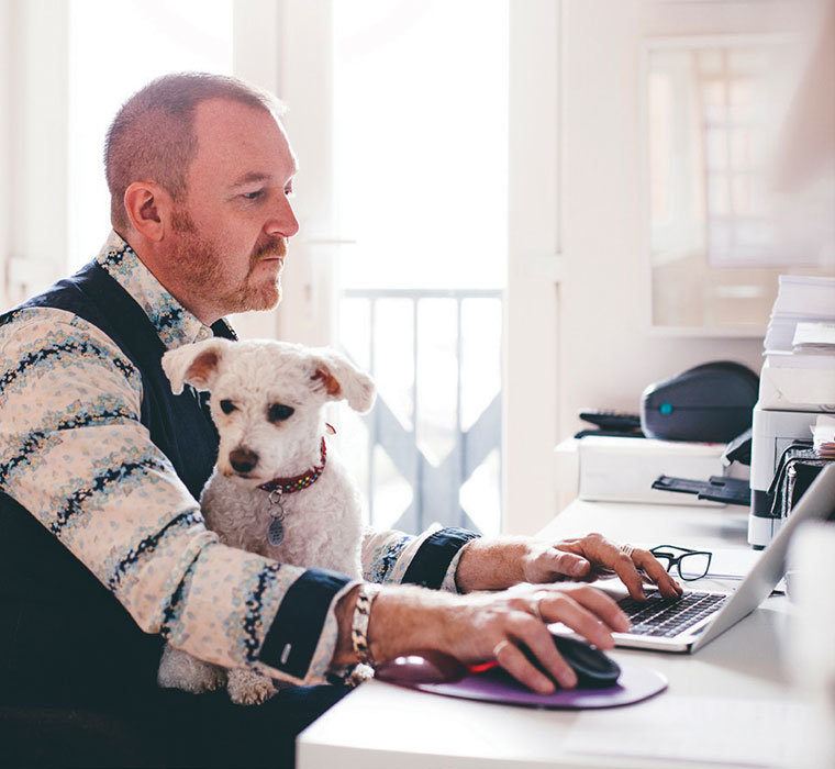 Mature man working from home in his studio office space with his dog sitting on his lap.