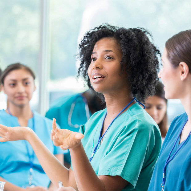 Student wearing scrubs asking a question among classmates