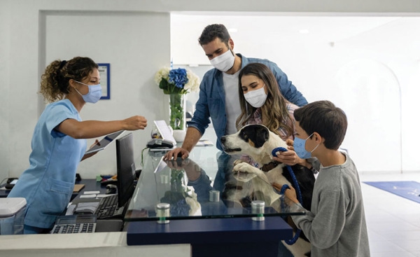 Happy Latin American family taking their dog to the vet wearing a facemask and puppy getting a treat from the receptionist